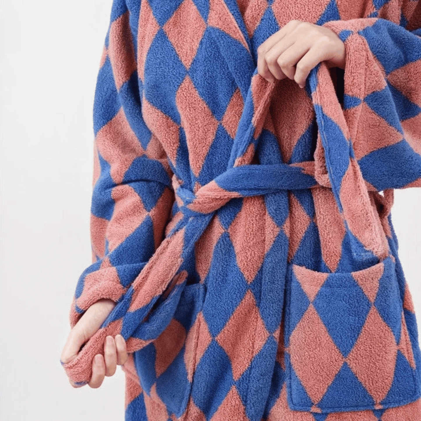 Blue and pink diamond patterned robe held by a person against a white background
