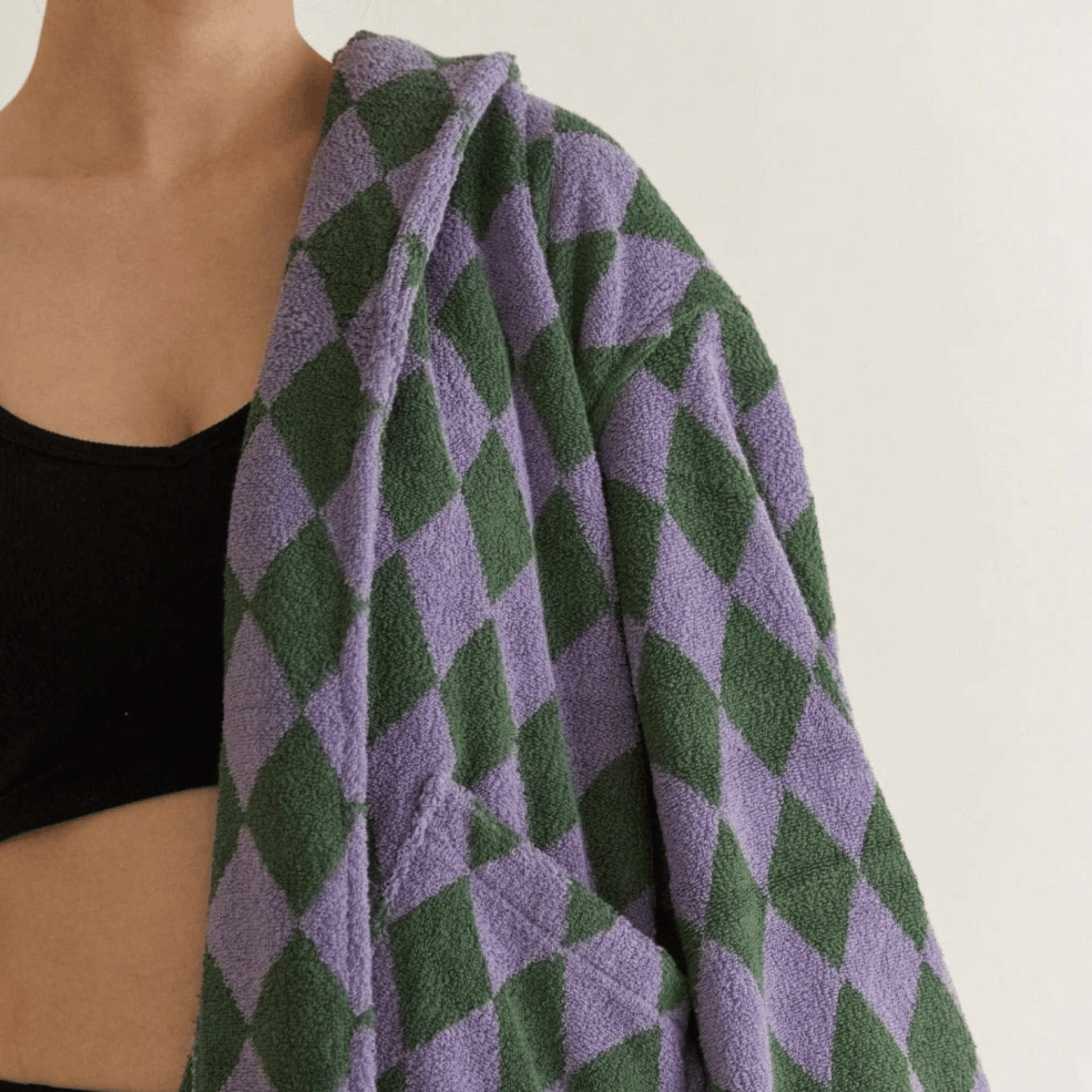 Person wearing a green and purple diamond patterned towel over their shoulder against a white background