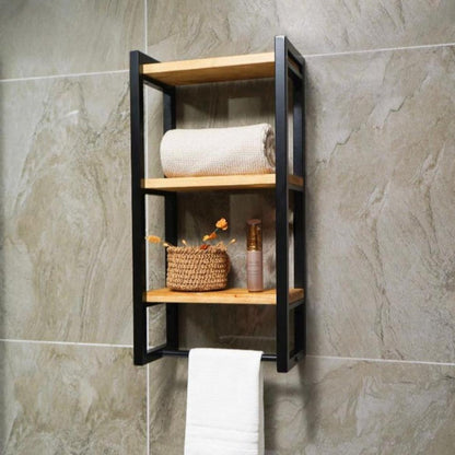 Three-shelf bath towel holder mounted on a stone wall, featuring black metal frames, wooden shelves, and displaying a rolled towel, decorative items, and a hanging towel.