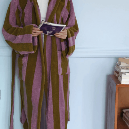 Person wearing a brown and purple striped robe holding a book against a light blue wall.