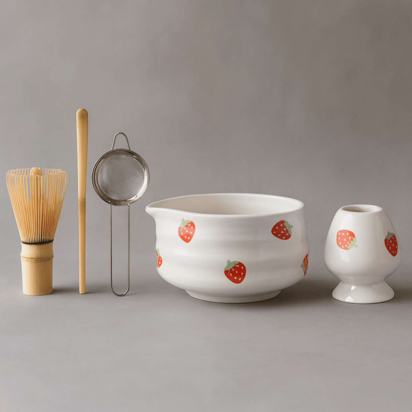 Ceramic bowl with strawberry pattern, whisk, and other tea-making tools on a gray background