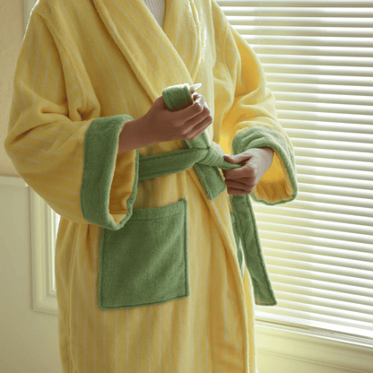 Person wearing a yellow and green robe holding a bottle of lotion.