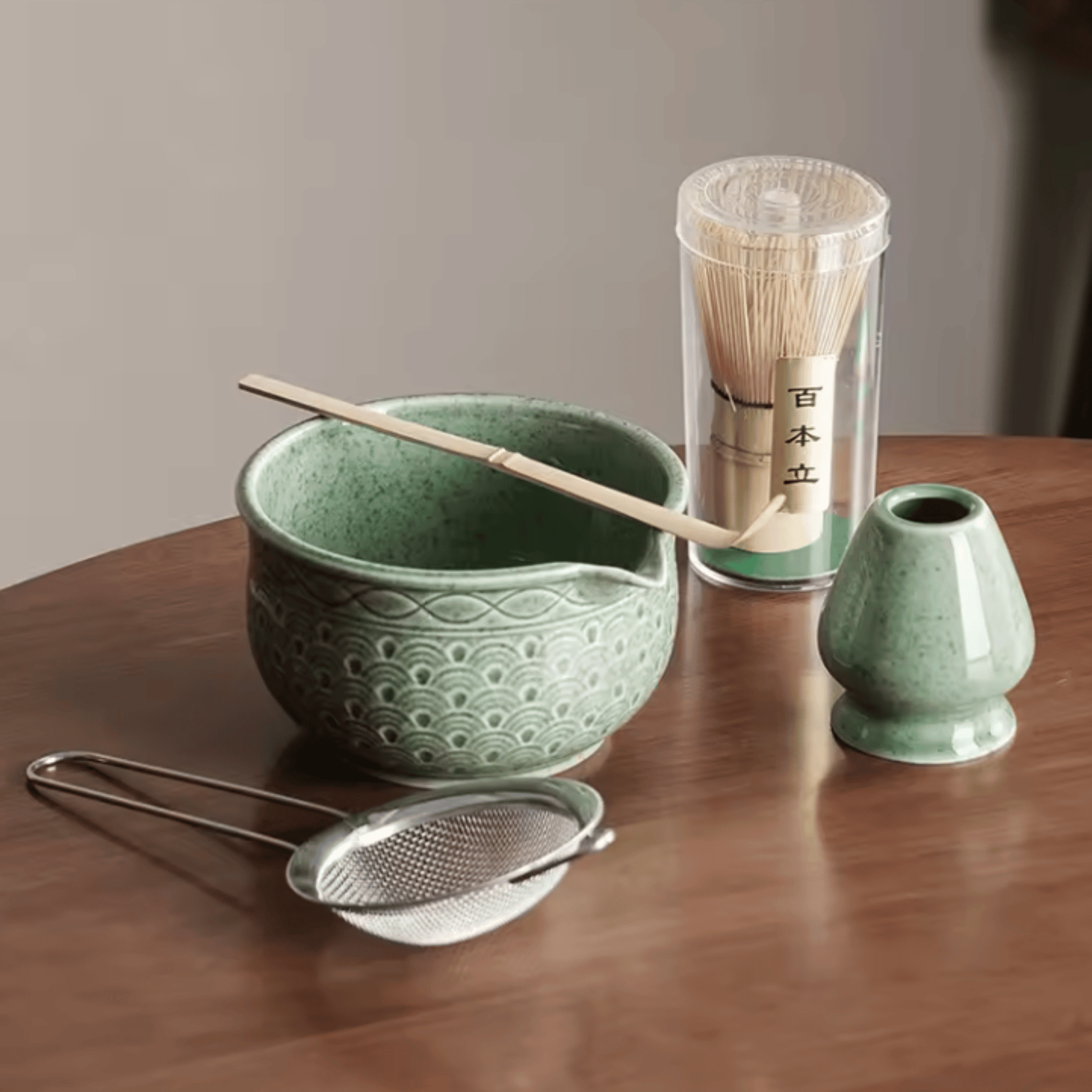 Green ceramic tea set with a bowl, whisk, scoop, and container on a wooden surface.