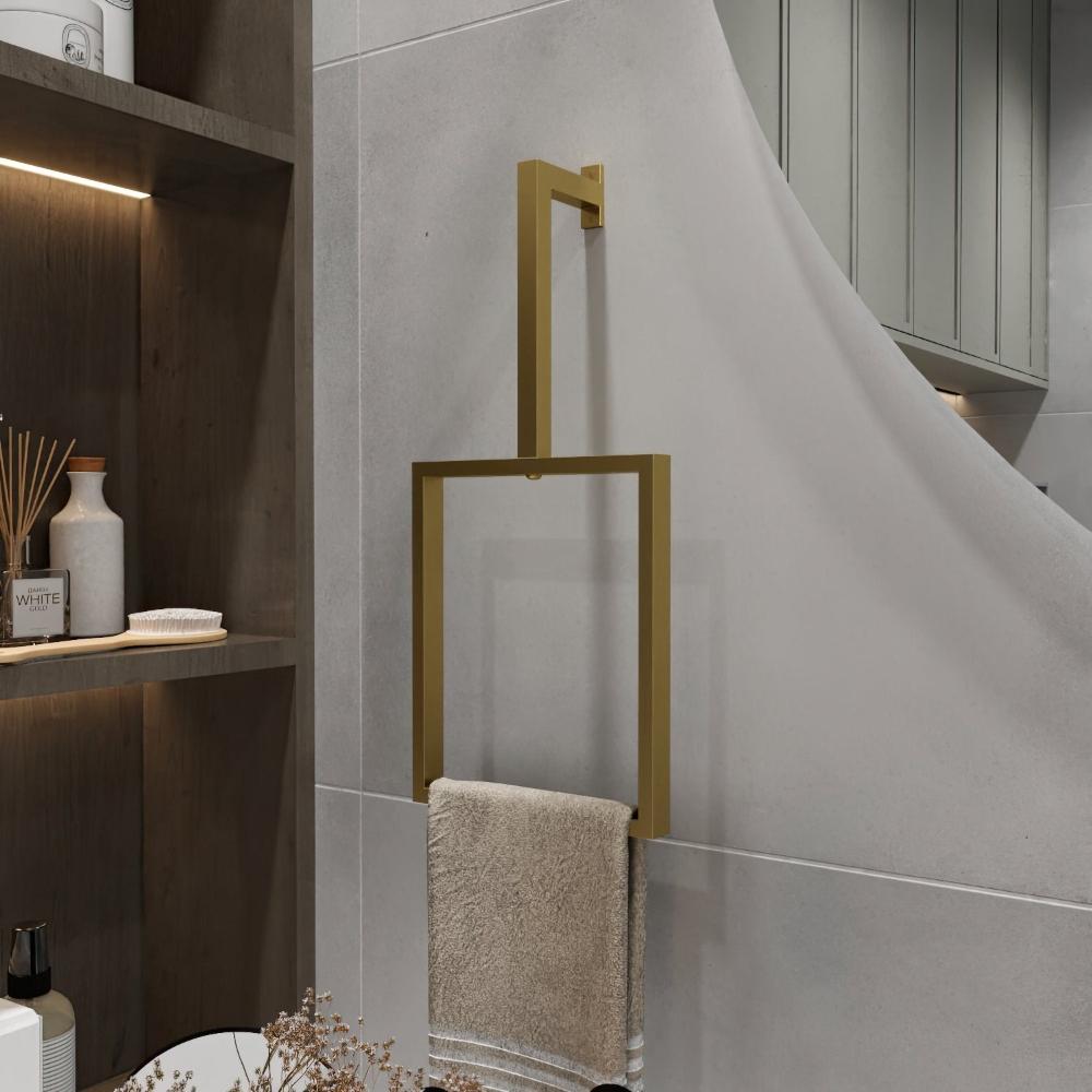 A minimalist gold-finished vertical towel ring is mounted on a light gray wall. The elegant rectangular design holds a beige towel, adding a luxurious touch to the bathroom decor.
