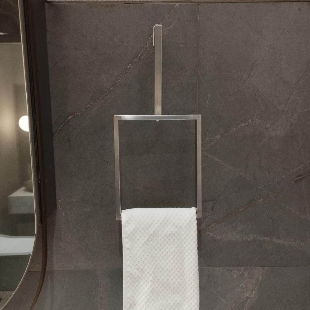 A minimalist vertical towel ring in a Satine Nickel finish is mounted on a dark stone wall. The sleek, rectangular design holds a white textured towel, adding a modern touch to the bathroom decor. The towel ring's simple yet elegant design complements the sophisticated ambiance of the space.